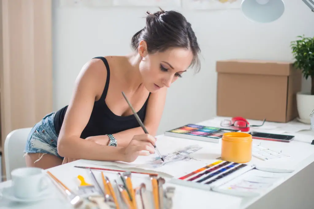 Woman working on hand-drawn art with her phone nearby to take a picture and turn it into an NFT.